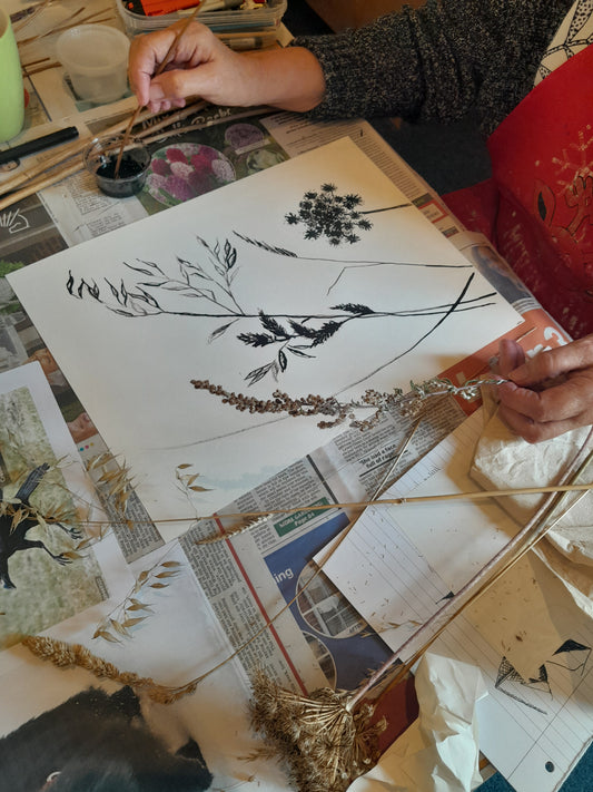 An art student drawing a plant on paper, surrounded by various art materials and reference images.