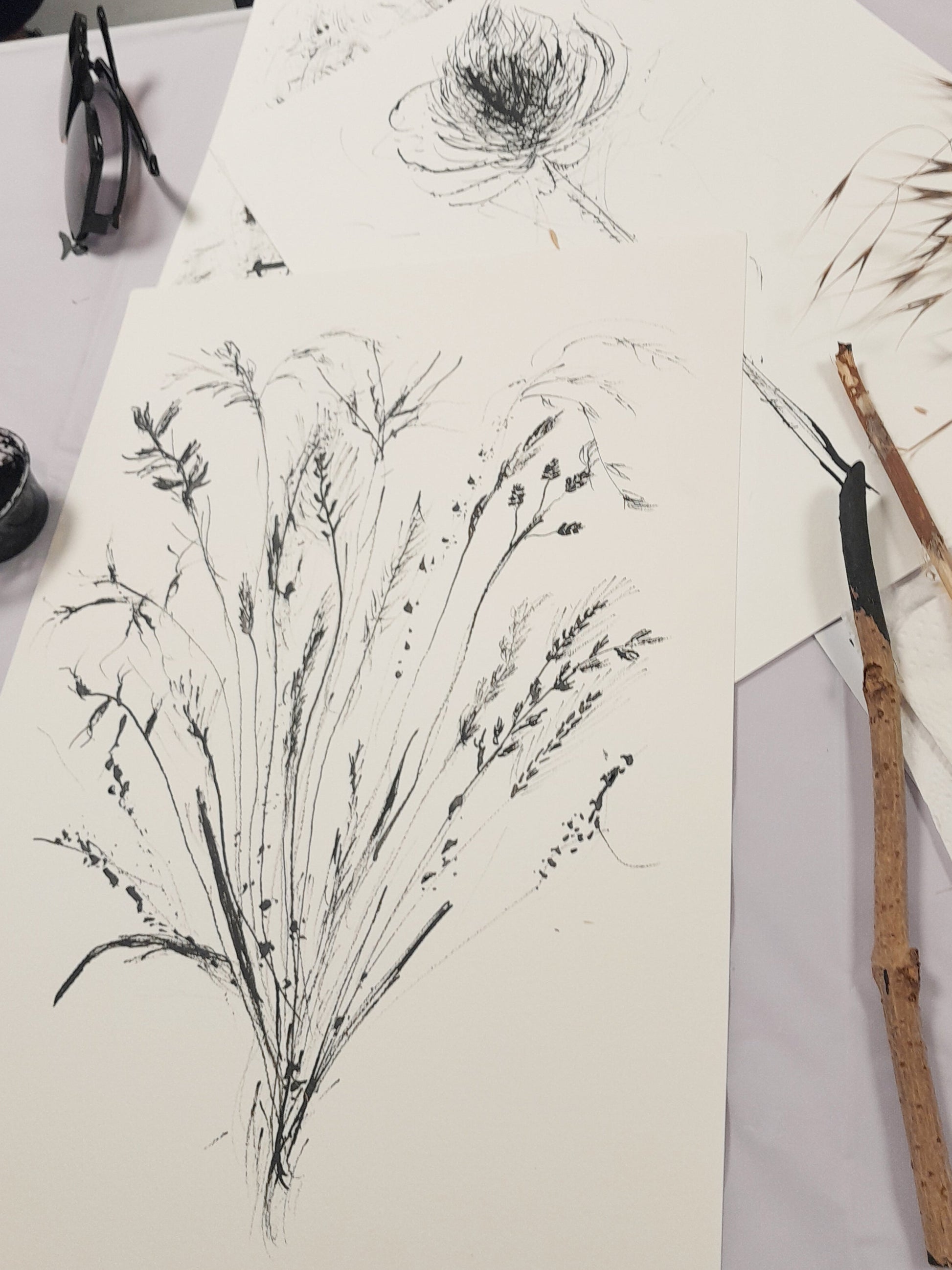 Artistic drawings of plants on paper with painting tools on a table.
